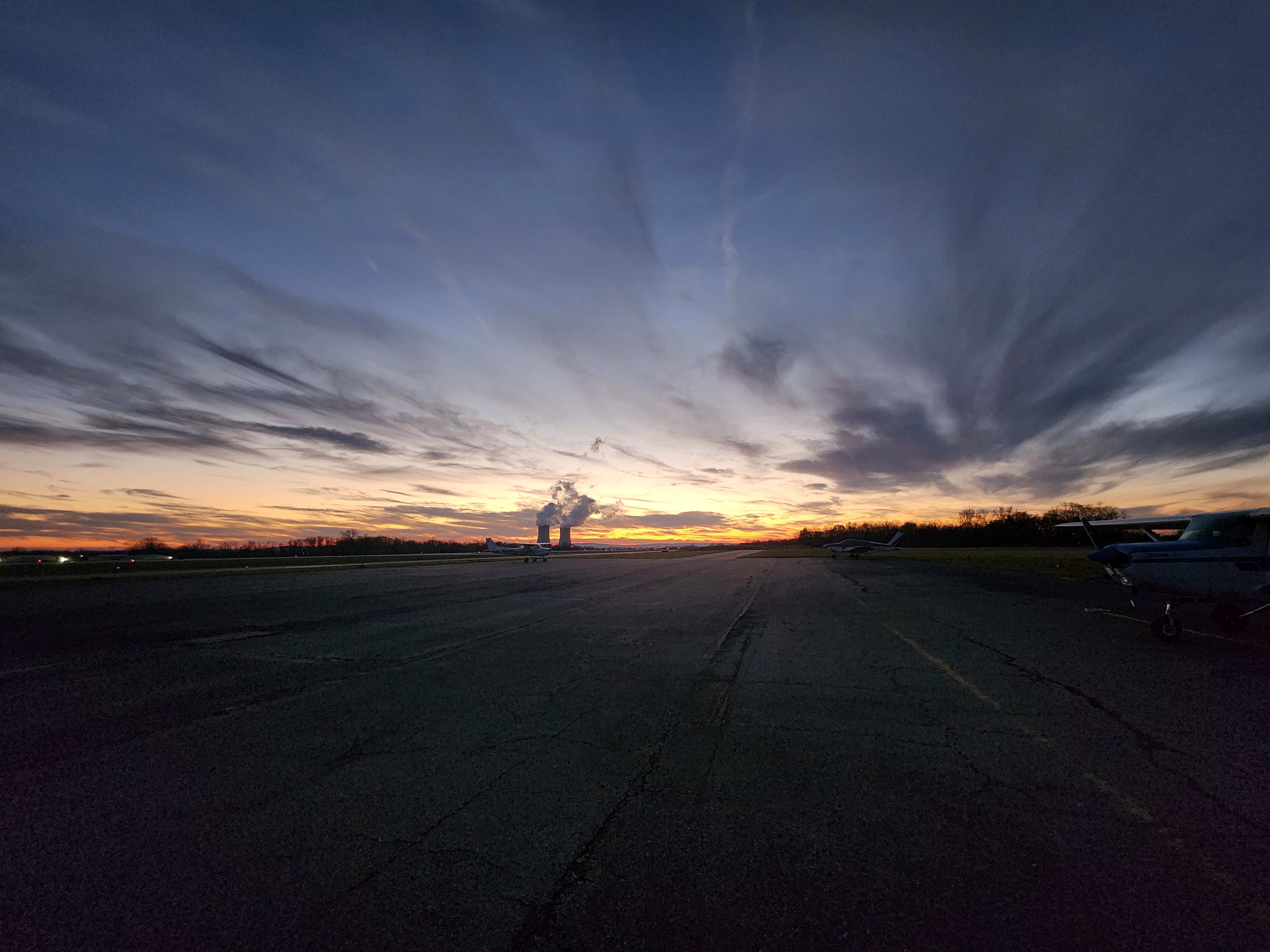 A wide airport apron at dusk with a Cessna parked at the edge and a colorful sky behind