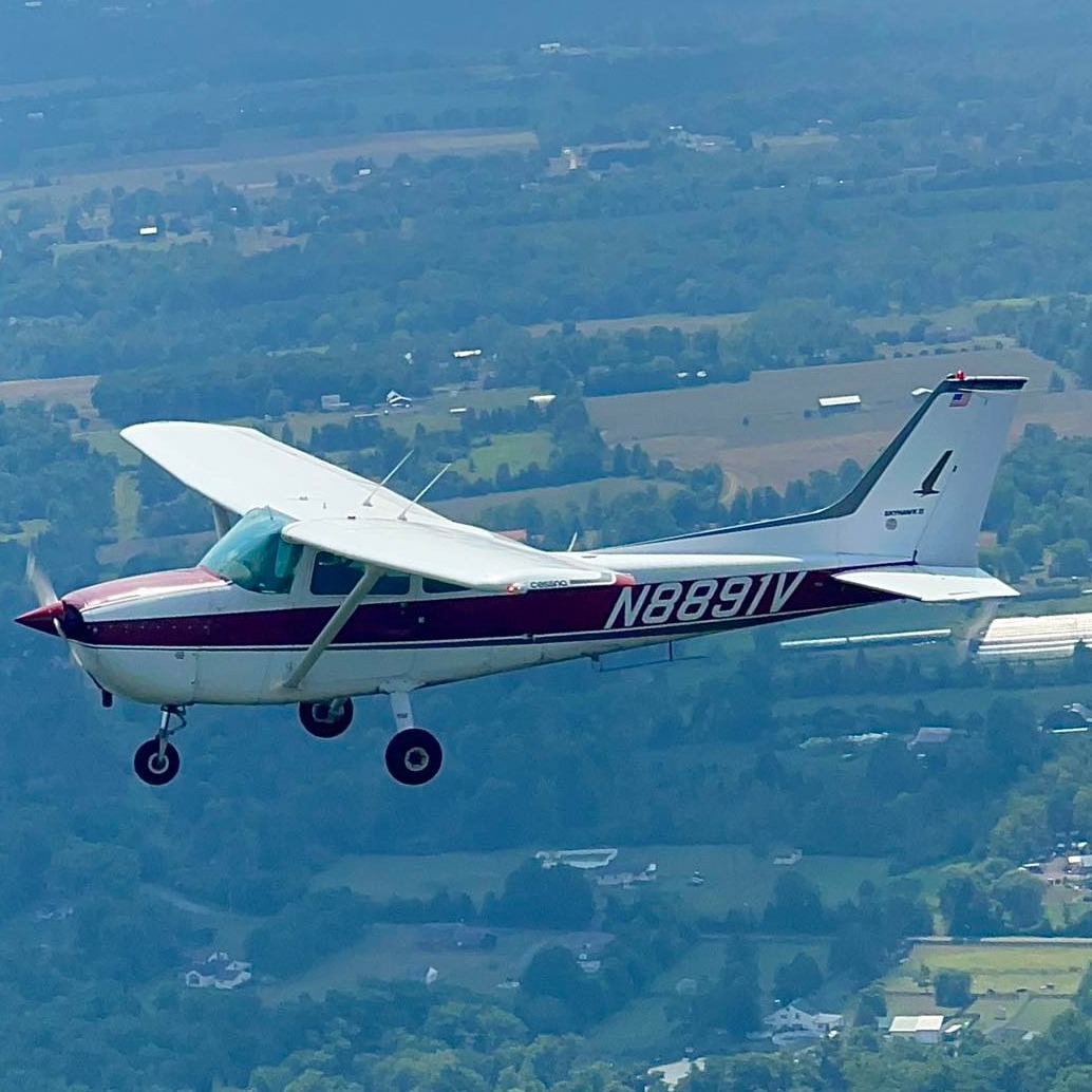 A Cessna 172 in flight over green countryside