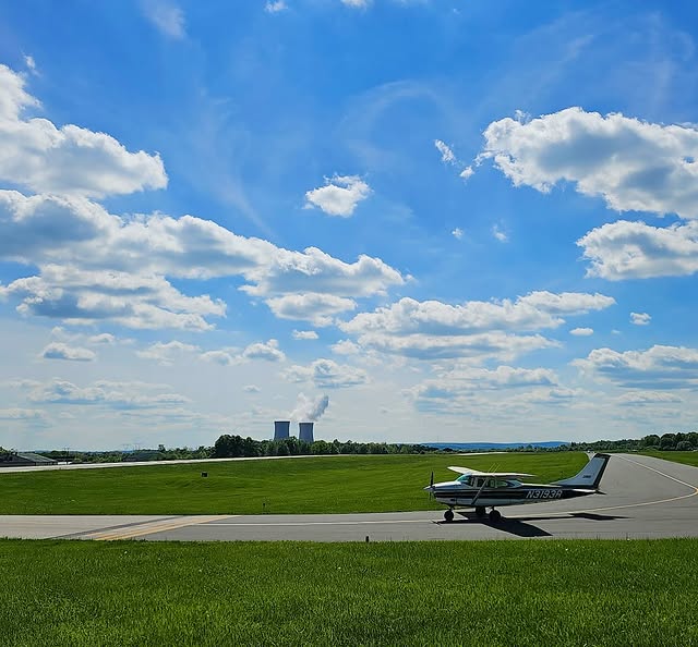 A small Cessna taxiing on an airport taxiway under a blue sky with clouds