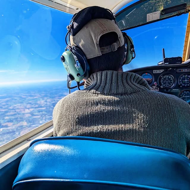 View from behind a person in a headset looking out of the cockpit window over land