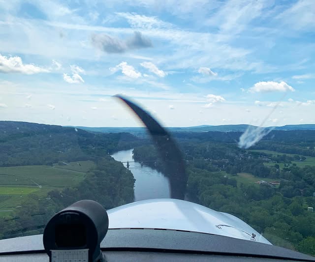 View over the nose and propeller of a river winding through green hills from the cockpit