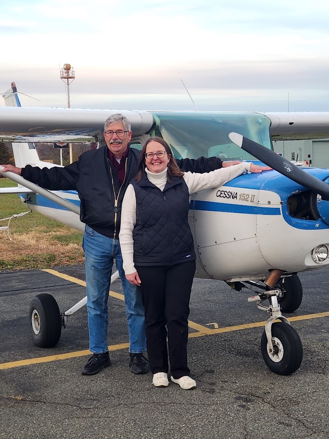Two people standing together beside a Cessna 152 on the ramp